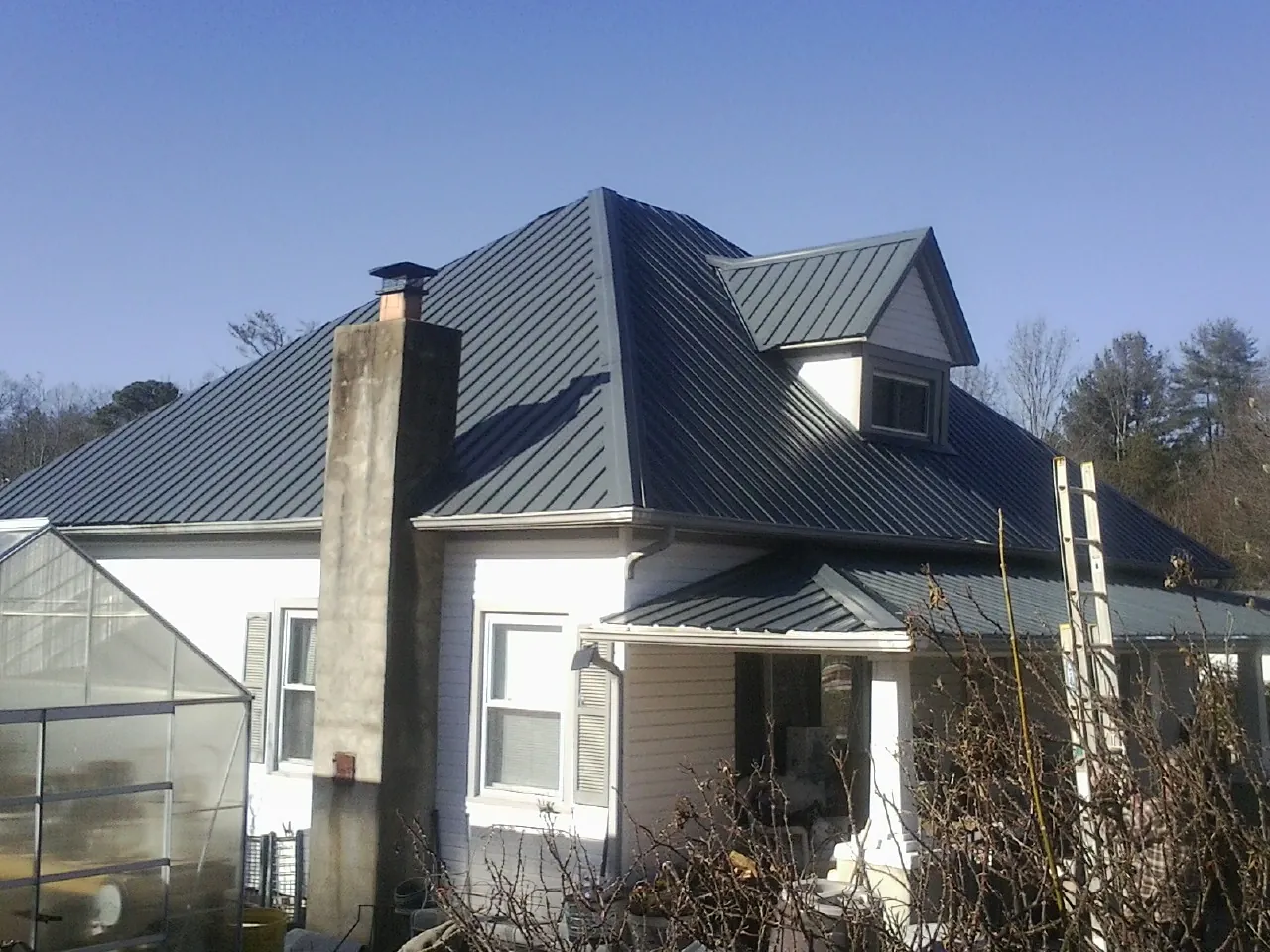 Dark blue standing seam metal roof on a white farmhouse with dormer — Slate & Tile Roof Repair by Roofing Brothers in Kaw City