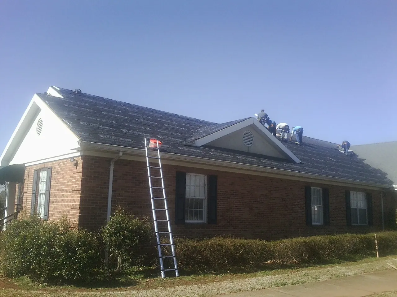 Crew tearing shingles off a brick ranch roof with a ladder set — Emergency Roof Repair work by our crew in Kaw City