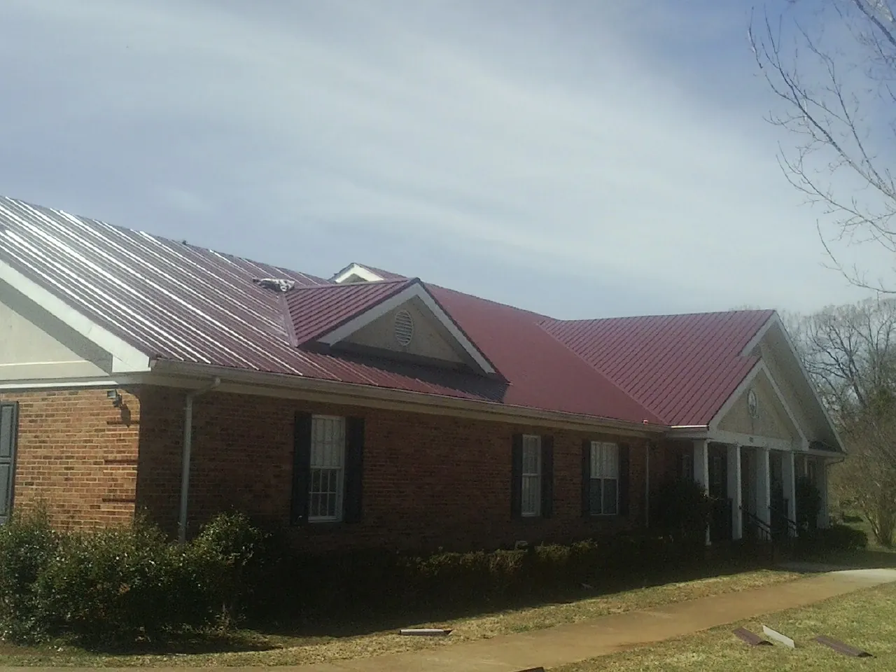 Red metal roof with gabled entries on a long brick building, from a Hail Damage Roof Repair job in Kaw City