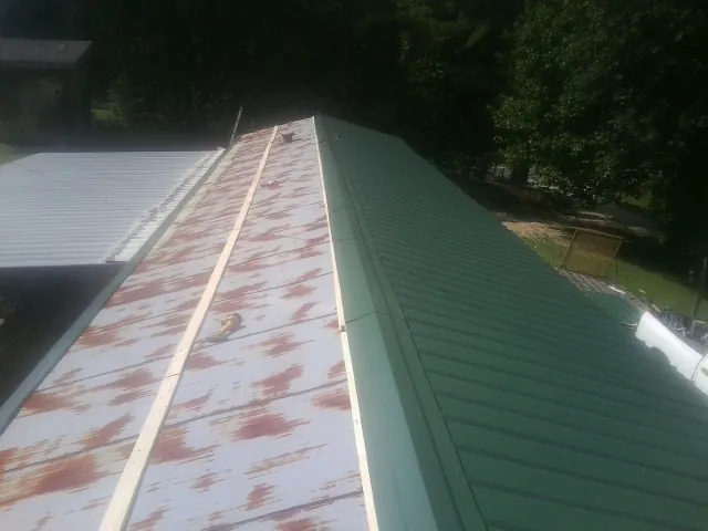 Old rusted panels beside newly installed green metal roofing — Wind Damage Roof Repair by Roofing Brothers in Kaw City