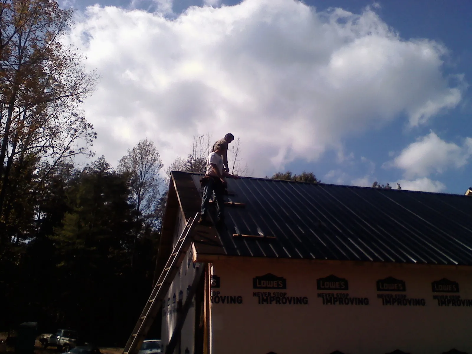 Roofer fastening dark metal panels high against a cloudy sky, from a Roof Inspection job in Kaw City