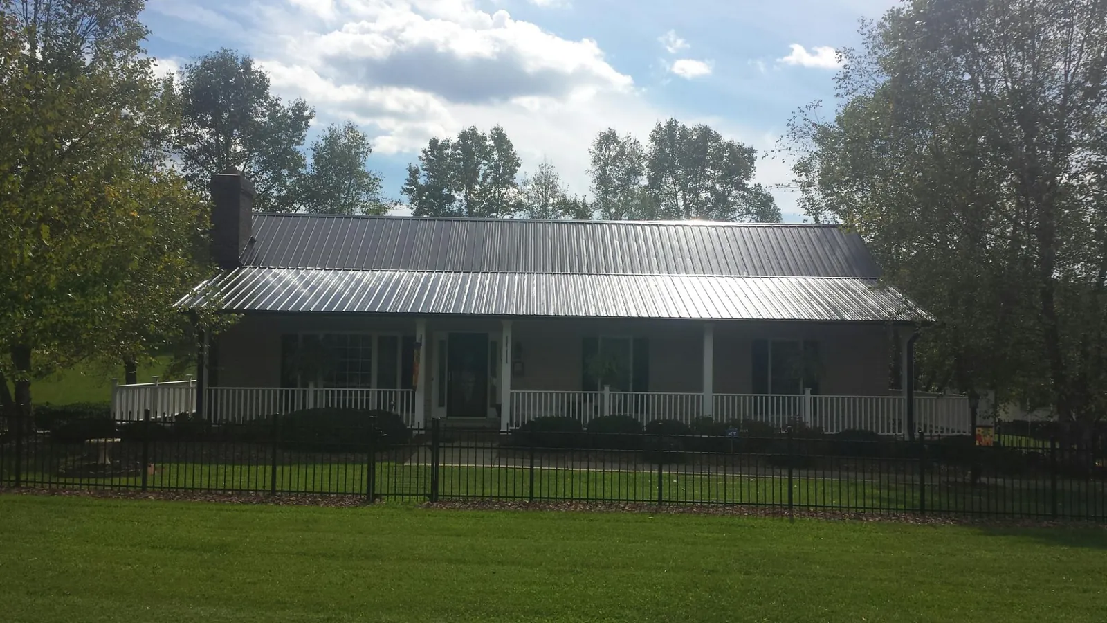 Gray metal roof on a brick ranch with a full width front porch — Gutter Guard Installation work by our crew in Kaw City