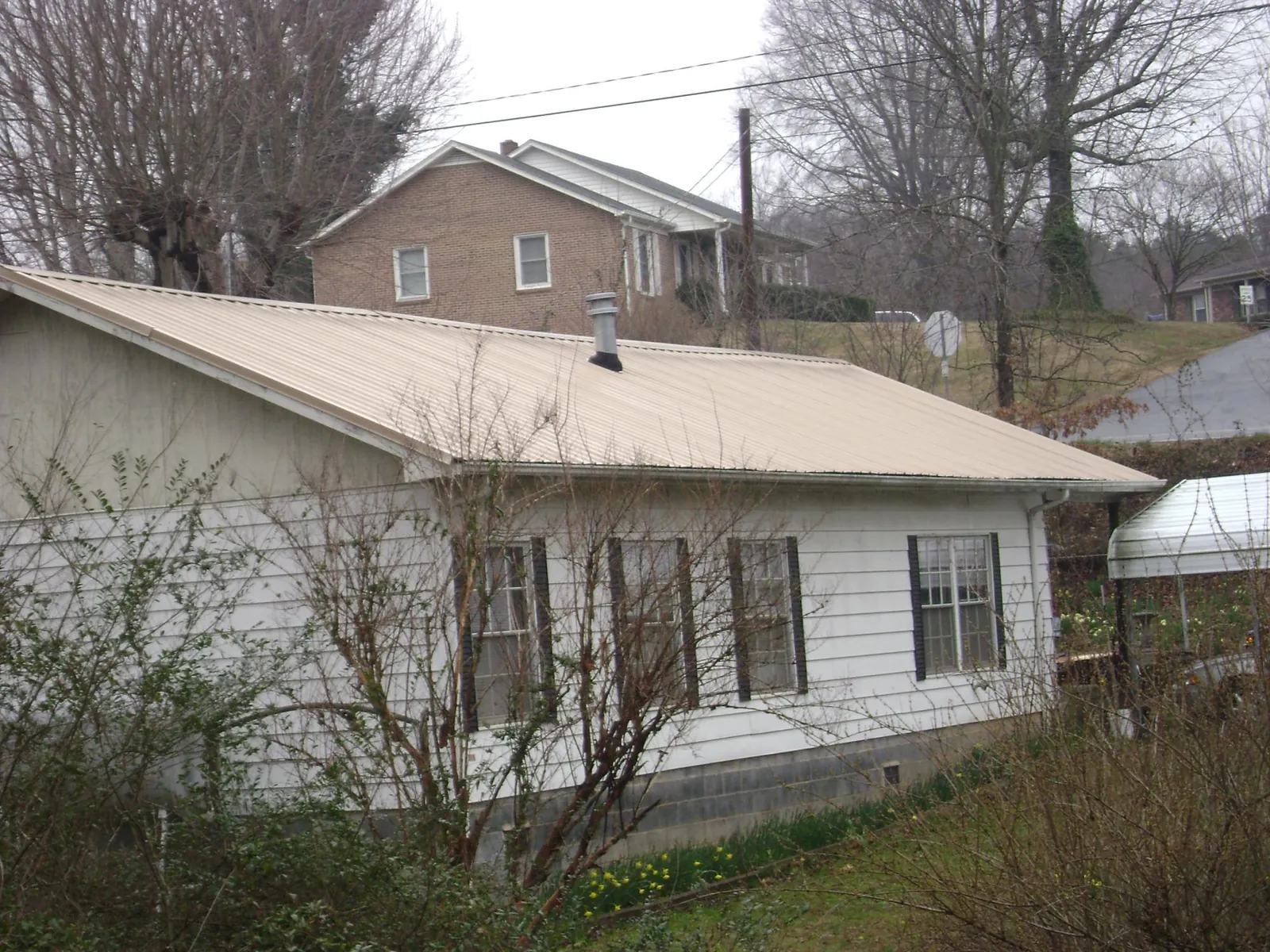 Tan metal roof on a white sided house set into a hillside — Commercial Roofing by Roofing Brothers in Kaw City