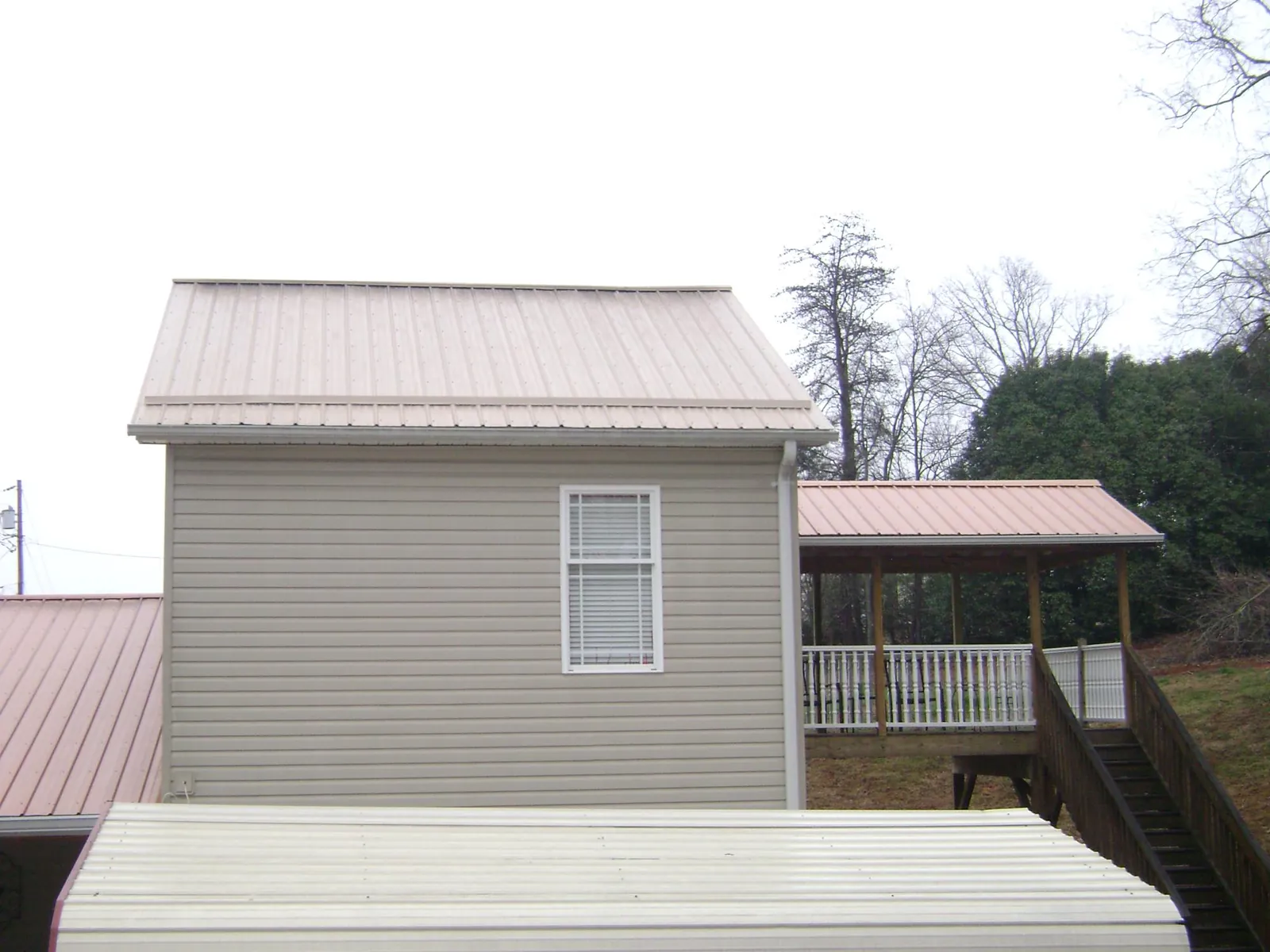 Tan metal roofs on a two story addition and attached porch, from a Roof Replacement job in Kaw City